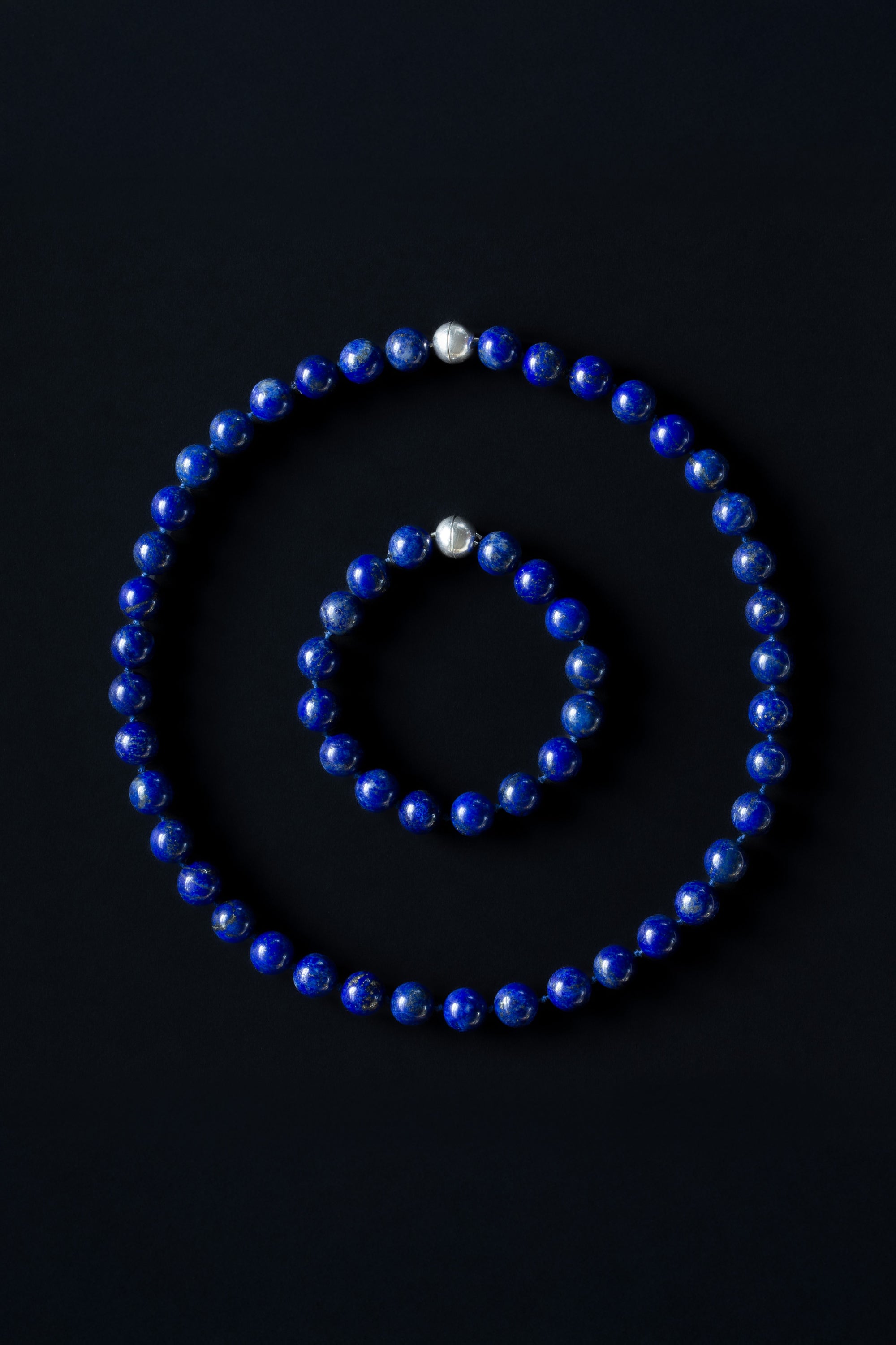 A set of lapis lazuli beaded necklace and bracelet with sterling silver magnetic clasps, displayed on a dark background.