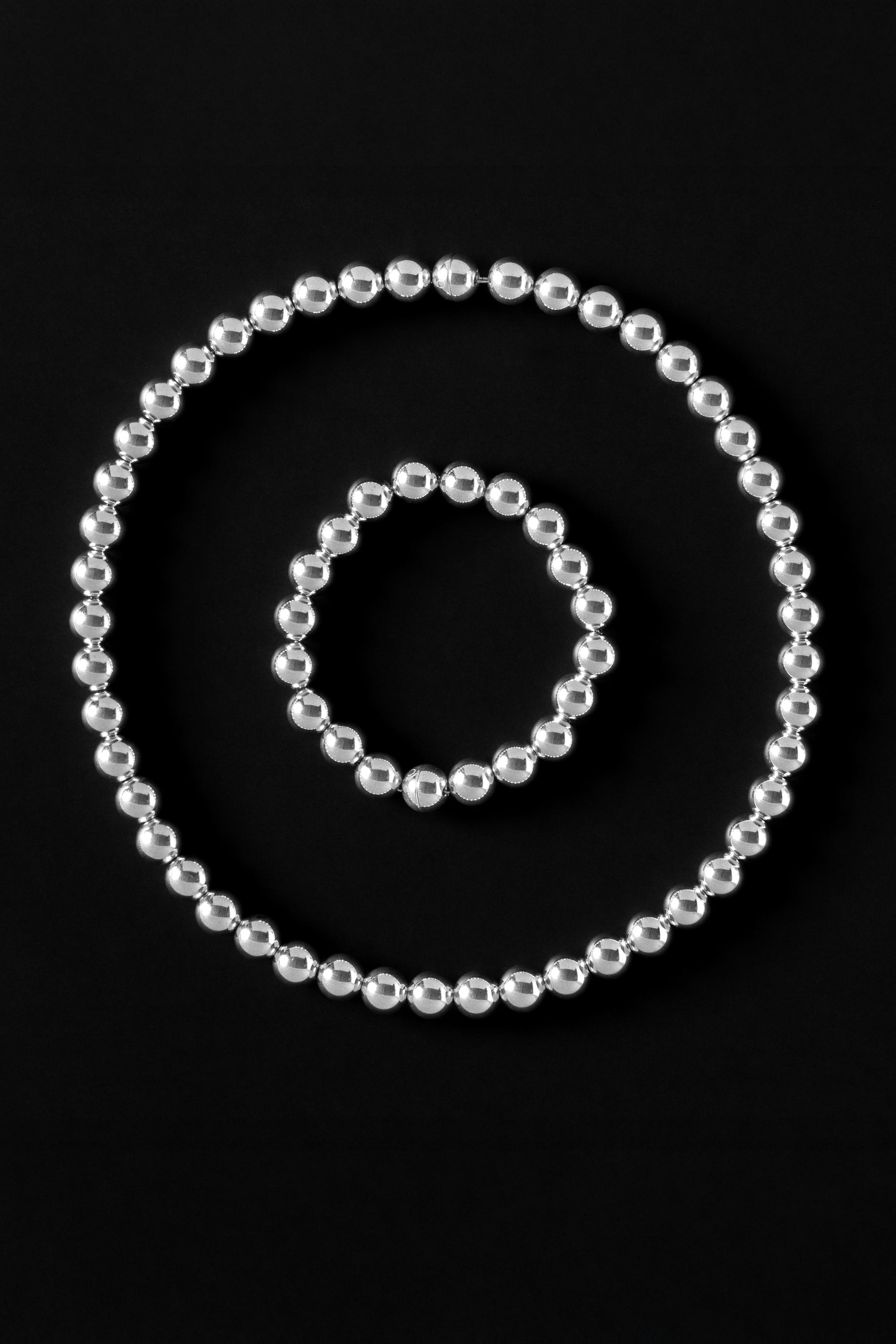 Set of silver beaded necklace and bracelets with magnetic clasp on a black background