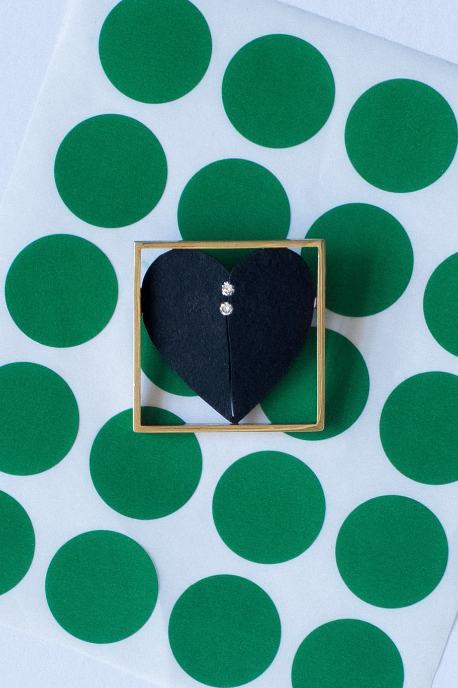Pat Flynn hand-forged textured iron heart brooch framed in 18k gold with two tension-set diamonds, front view on green stickers