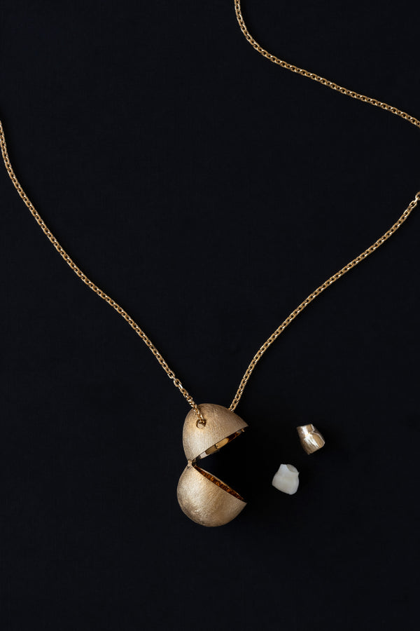 Egg shaped locket vessel necklace in 18k yellow gold open with Childs good milk tooth